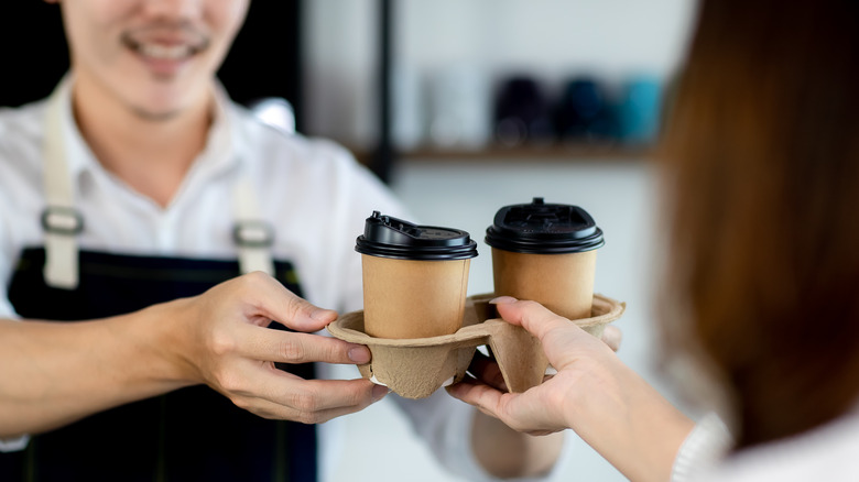 Barista handing woman coffee cups