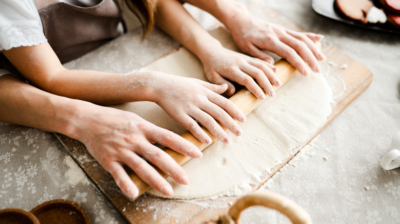 Two sets of hands roll out dough