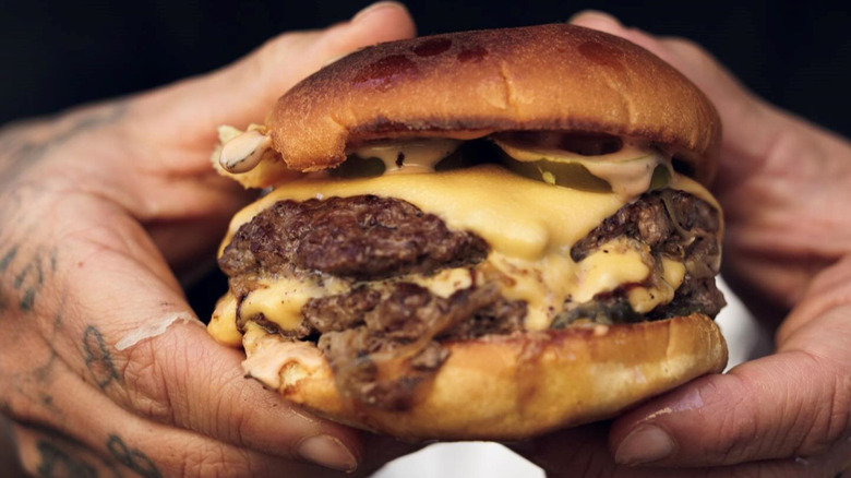 Close-up of hands holding NADC burger with cheese and two patties