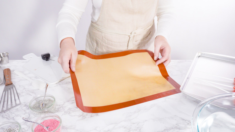 hands hold up silicone food mat above marble counter