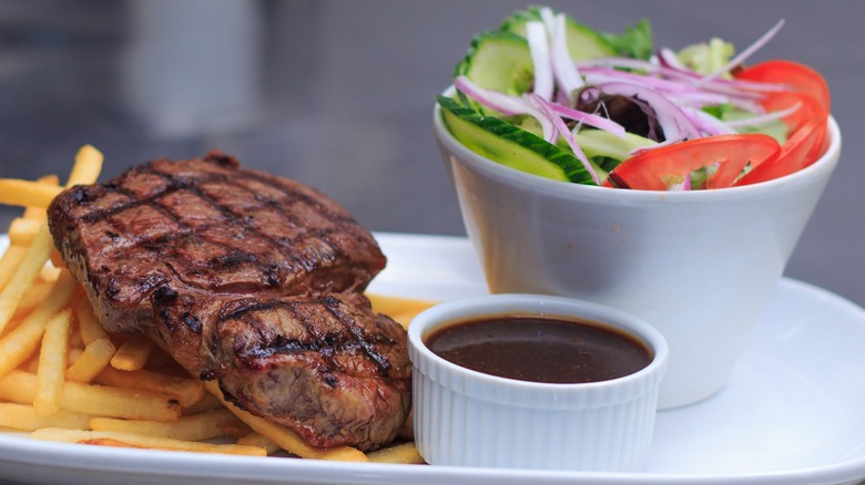 A steak, fries, and salad with a dish of steak sauce