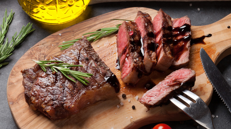 Sliced steak with brown sauce on a wooden cutting board