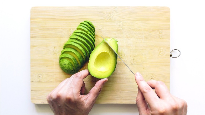 Hand slicing avocado on cutting board 