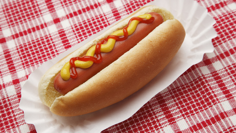 Hot dog with ketchup and mustard in a paper cup on a red-and-white checkered table