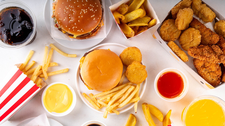 Fast food burger, chicken sandwich, nuggets, sodas, fries on a white table.