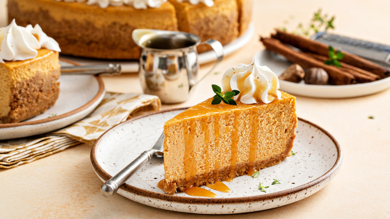 A slice of pumpkin cheesecake with caramel glaze and whiped cream in festive setting