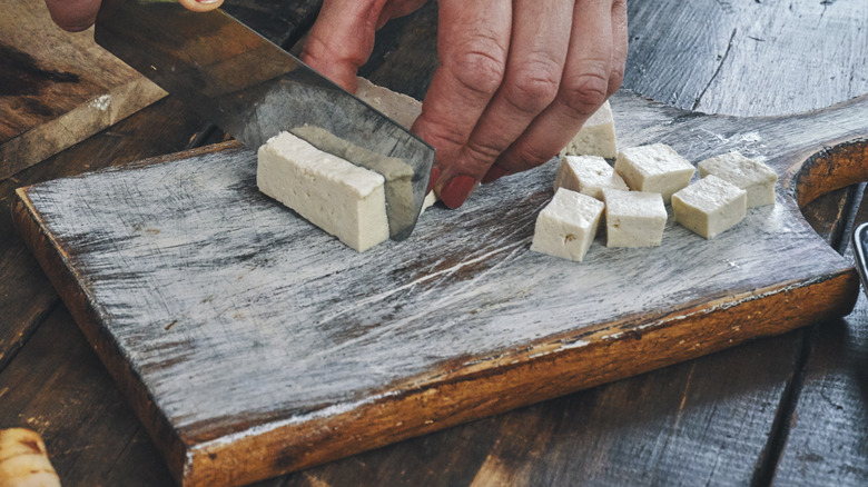 hand chopping tofu into cubes with knife