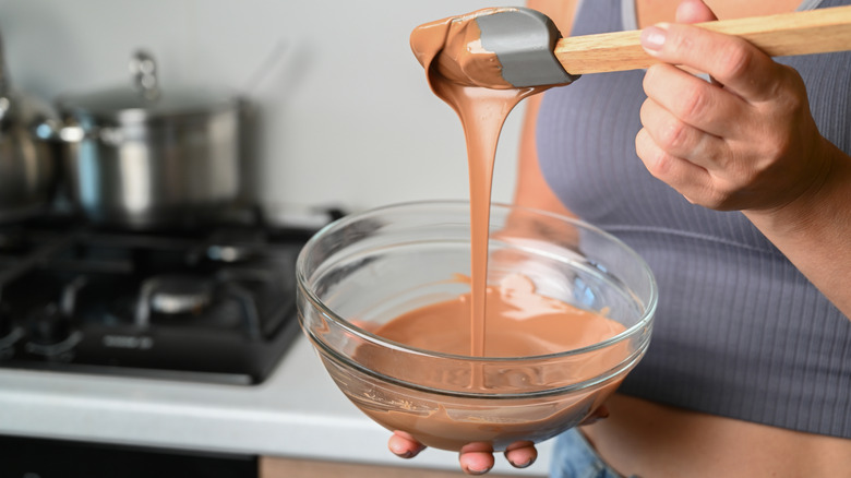 Melted chocolate dripping from spatula into a glass bowl