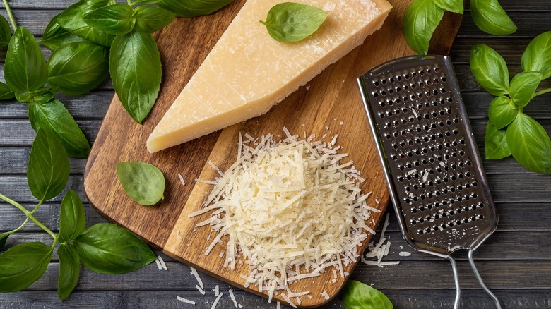 grated parmesan with parmesan wedge and grater on a wood cutting board