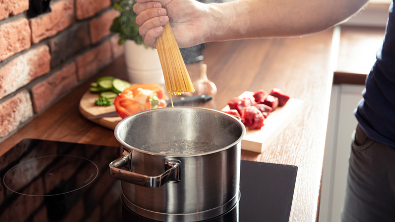 Hand adding spaghetti to pot