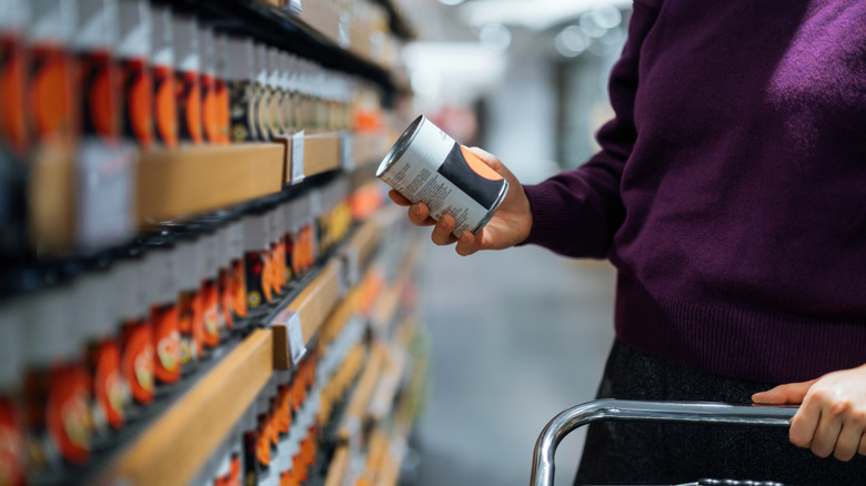 Man with shopping cart holding can in grocery aisle