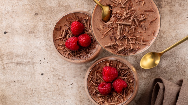 Three portions of chocolate mousse topped with chocolate shavings and raspberries