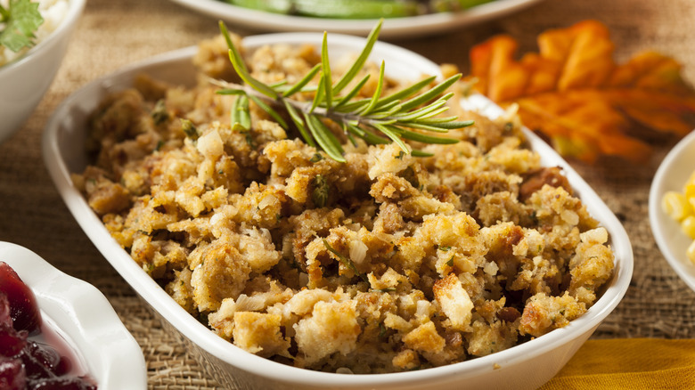 A dish of homemade stuffing on a Thanksgiving table with a rosemary garnish