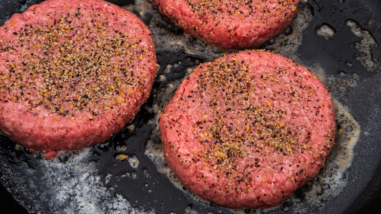 Seasoned burgers sizzling in cast iron