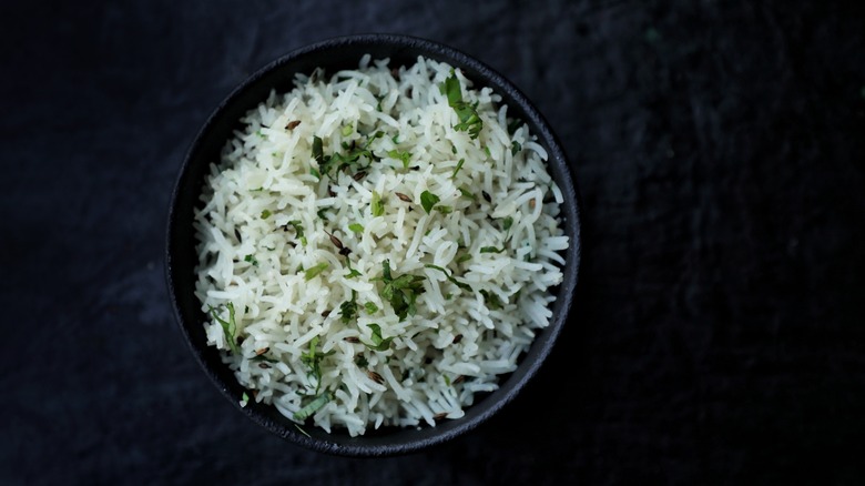 Bowl of cooked basmati rice with herbs and cumin seeds.