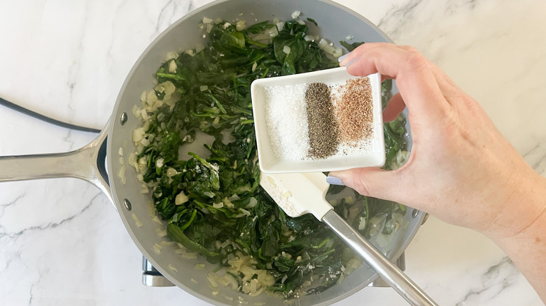 hand adding seasonings to spinach