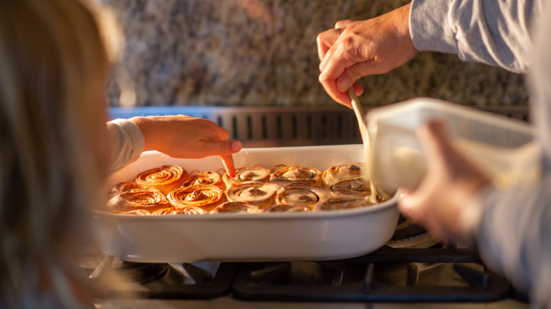 Two people glaze cinnamon rolls