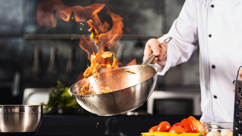 Professional chef holding a sizzling pot with fire 