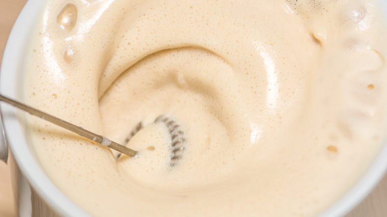 Metal frothing tool in coffee-colored milk foam