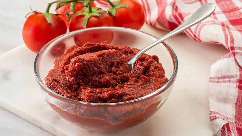 Tomato paste in glass bowl with vine tomatoes and a dish rag