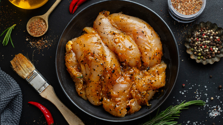 Marinated raw chicken on black plate.