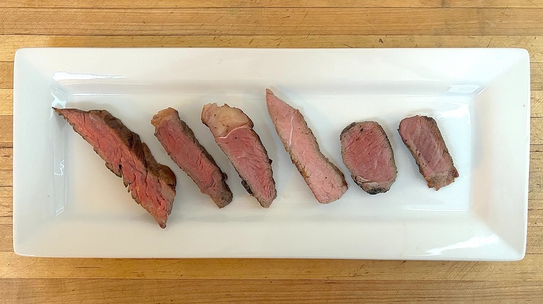 Assorted slices of cooked Aldi steaks on white, rectangular plate