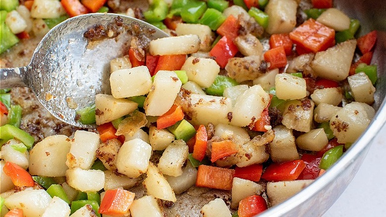 spoon stirring potatoes and bell peppers in skillet