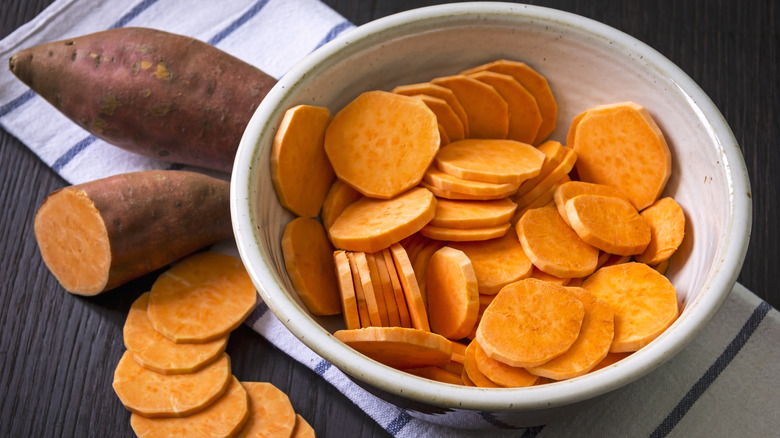 Bowl of sweet potato slices sitting by sweet potatoes