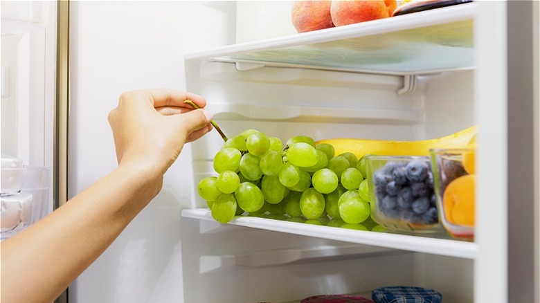 Hand removing green grapes from refrigerator 