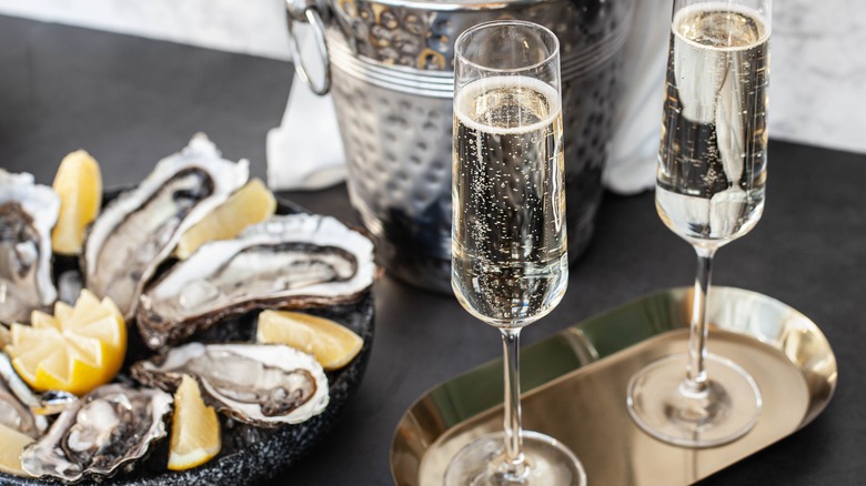 two glasses sparkling wine on tray near a plate of oysters 