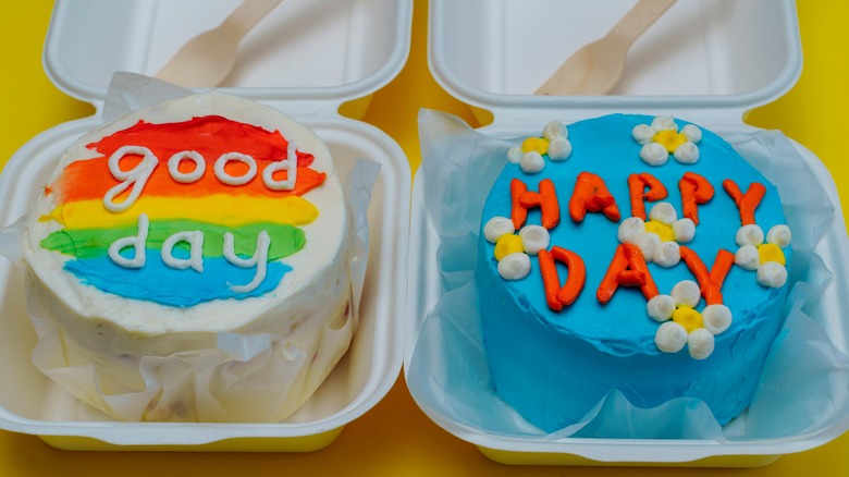 Two bento cakes in boxes, one rainbow and one blue