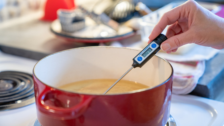 Person using a thermometer to check the temperature of oil in a Dutch oven