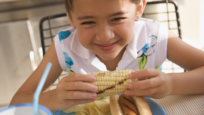 Young girl eating corn at home