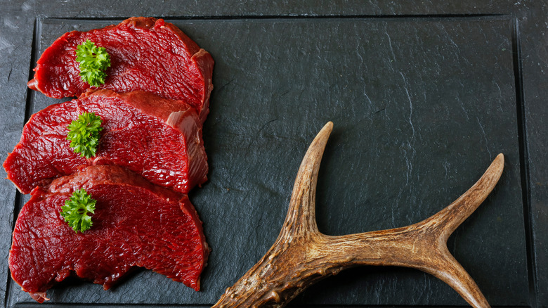 Venison steaks and antlers on a black tile