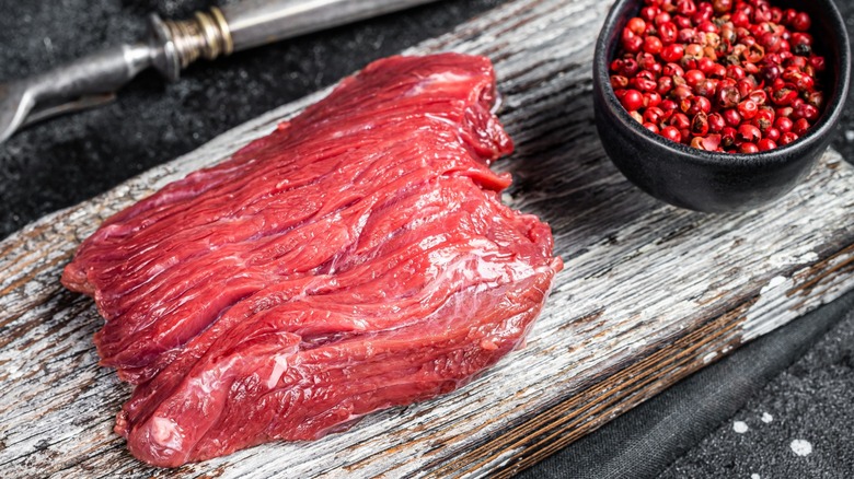 Raw venison steak and peppercorns on a board