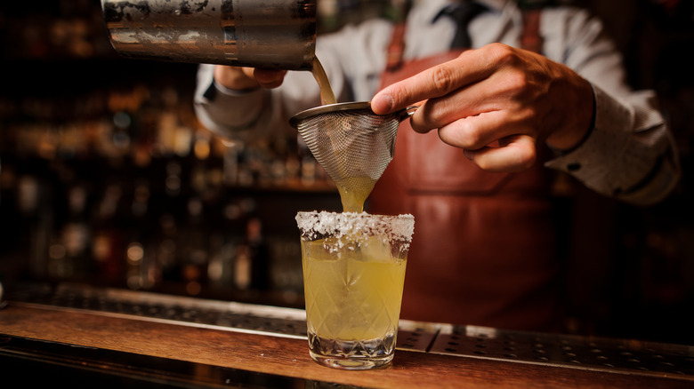 Bartender pouring drink through strainer into glass