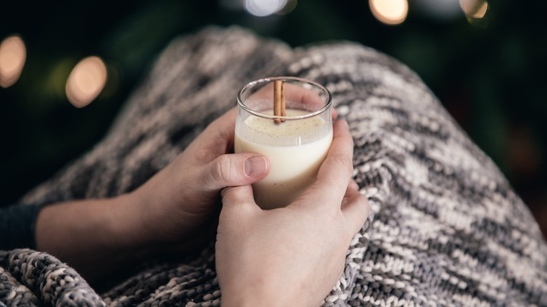 Person covered in a blanket holding a cup of eggnog