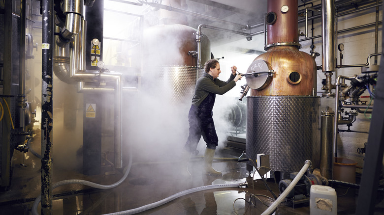 View of a modern distillery, with a worker checking a machine, surrounded by steam