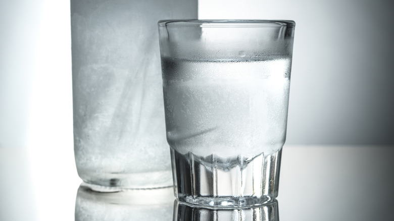 Close-up of shot glass with clear alcohol in it, with frozen bottle in background