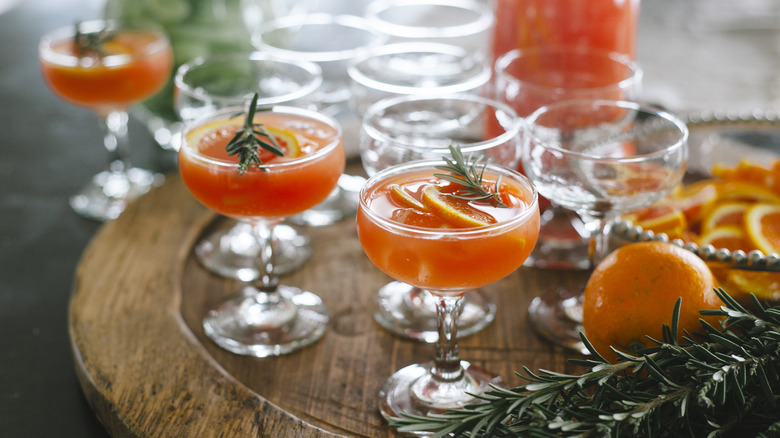 Multiple glasses of an orange cocktail, garnished with orange slices and rosemary sprigs