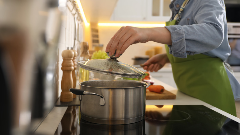 Pot boiling water on stovetop woman lifting lid