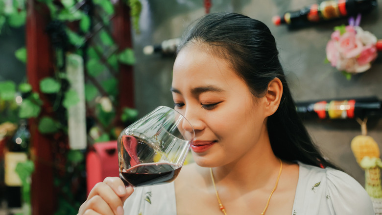 Person smelling red wine in a glass.