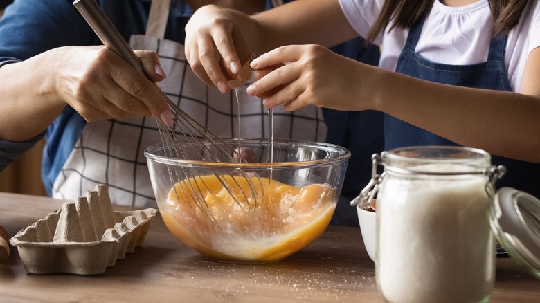 Two people crack eggs into bowl