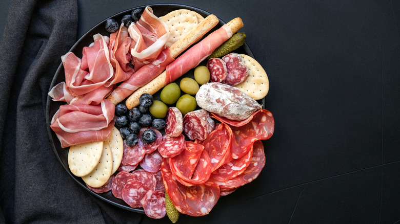 A plate of charcuterie with crackers, olives, an blueberries