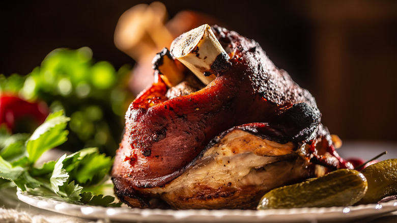 Roasted pork knuckle with pickles and greens on a plate