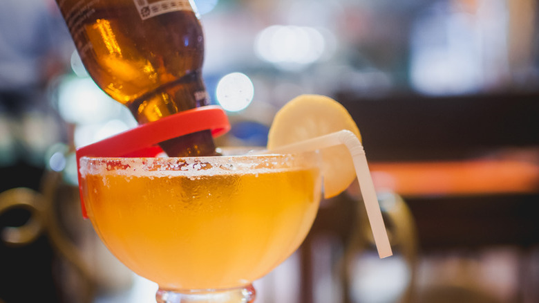 Pouring a bottle of beer into a salt-rimmed glass with a straw and a lemon garnish