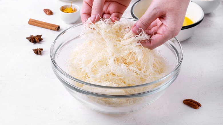 Hands taking apart knafeh dough