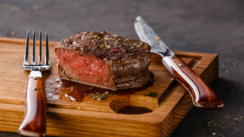 A juicy steak on a wooden cutting board with knife and fork