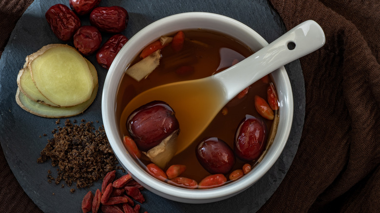 Jujube fruit in a bowl with dried jujube fruits, ginger, and spices surrounding the bowl