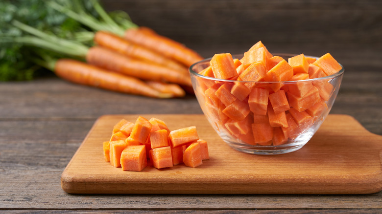 Diced carrots in glass bowl, with more piled on wooden cutting board